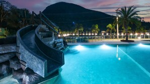 A swimming pool with a stone staircase leading up to a viewing platform, surrounded by palm trees and a mountain in the background. -  Art Green (Teresópolis)