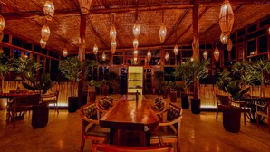 A restaurant with a long wooden table and chairs, surrounded by potted plants and hanging lights. -  Art Green (Teresópolis)