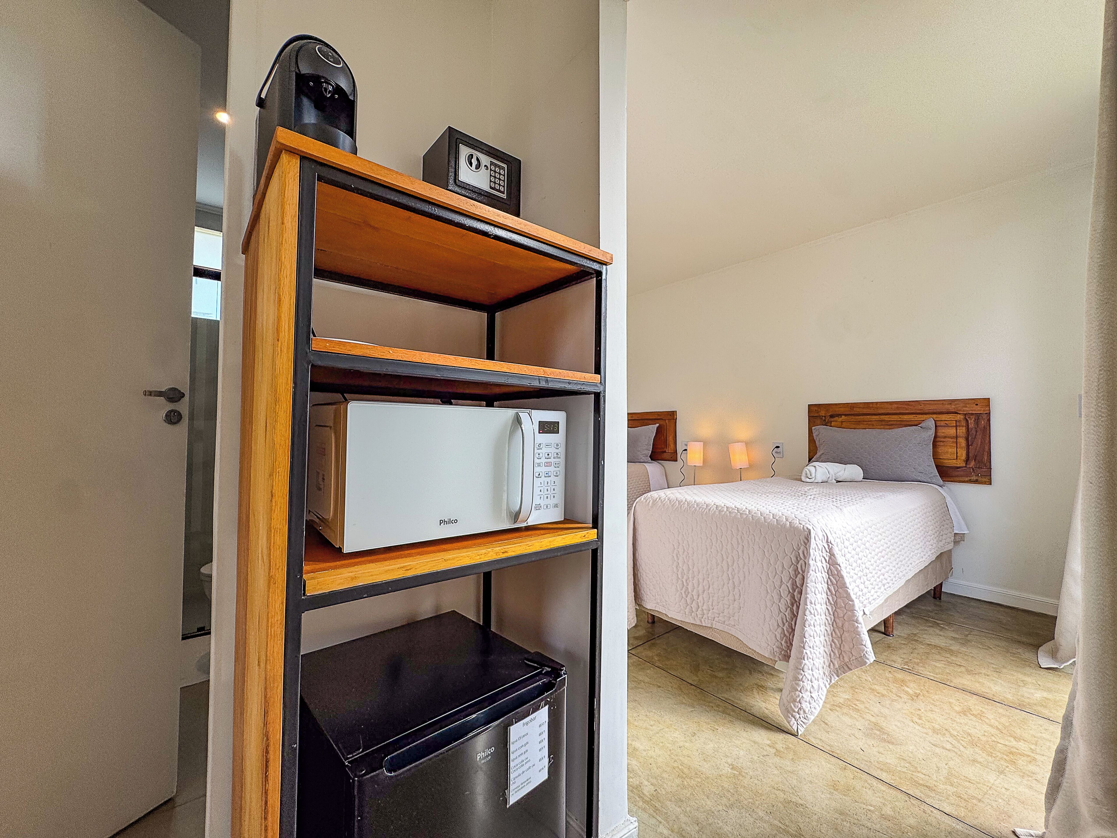 Une chambre d’hôtel avec un lit, des lampes de chevet, une étagère en bois avec un four à micro-ondes et un meuble noir.