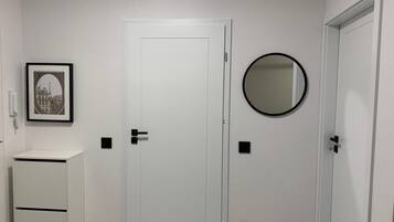 A room with a white door, a small white cabinet, a framed picture, and a round mirror on the wall.