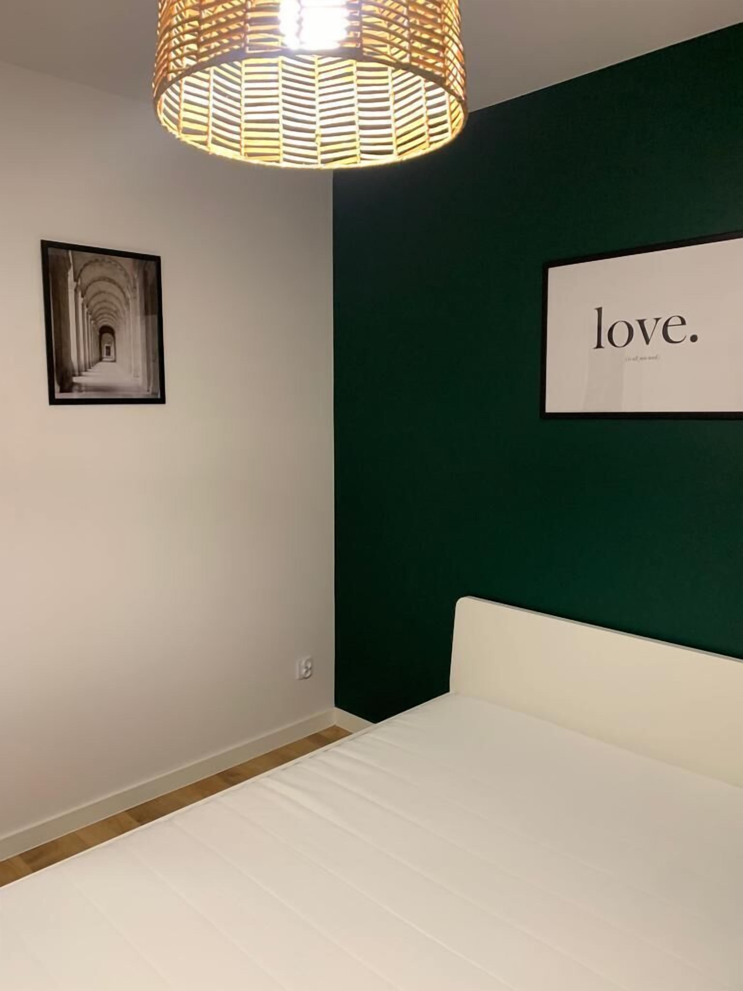 A bedroom with a bed, a hanging light fixture, a framed picture on the wall, and a sign with the word "love."