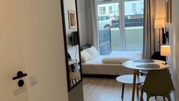 Habitación de hotel con cama, escritorio, silla, ventana con vistas a edificios y puerta.