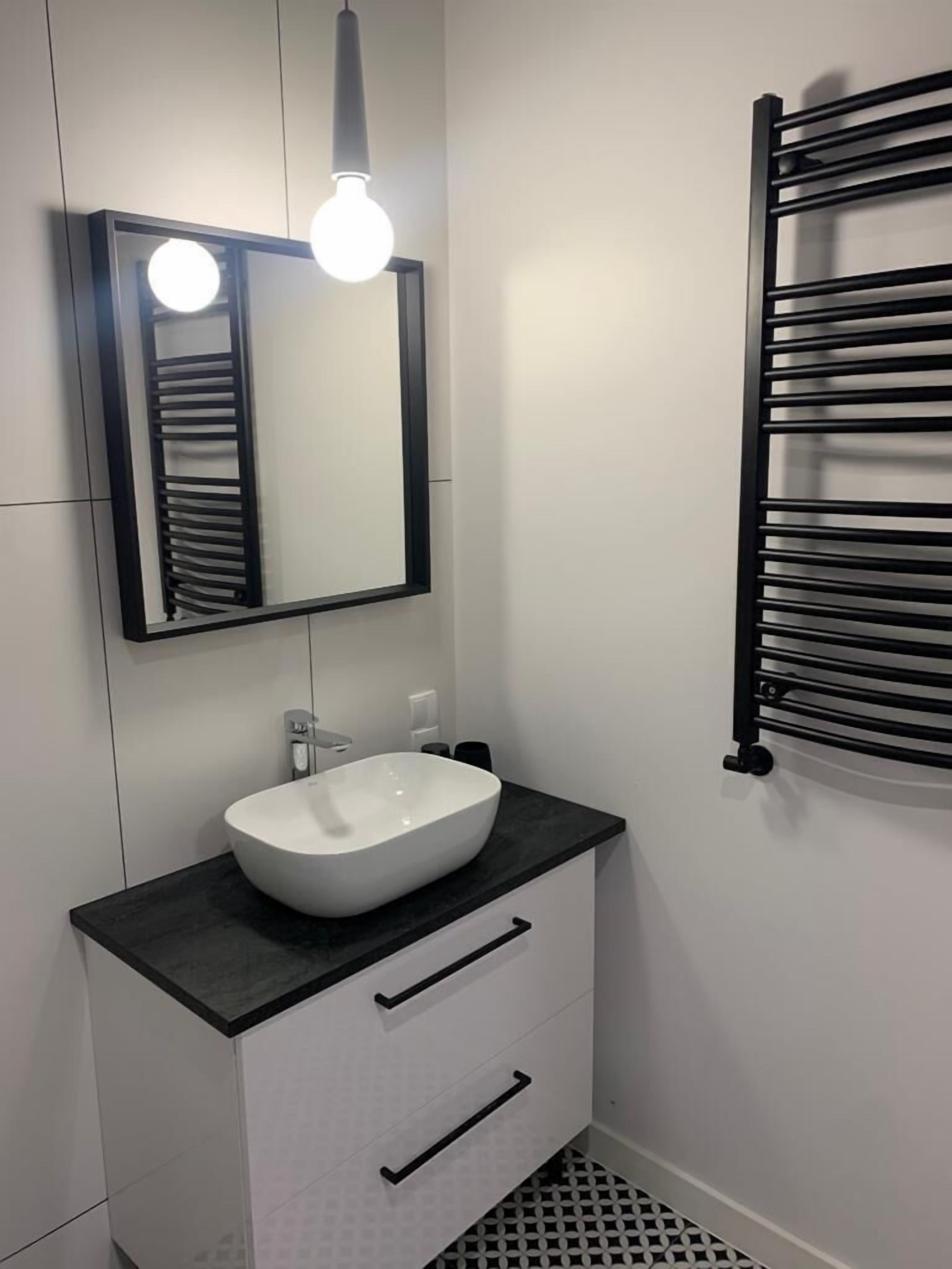 A modern bathroom with a white sink, black countertop, and a mirror with a light fixture above it.