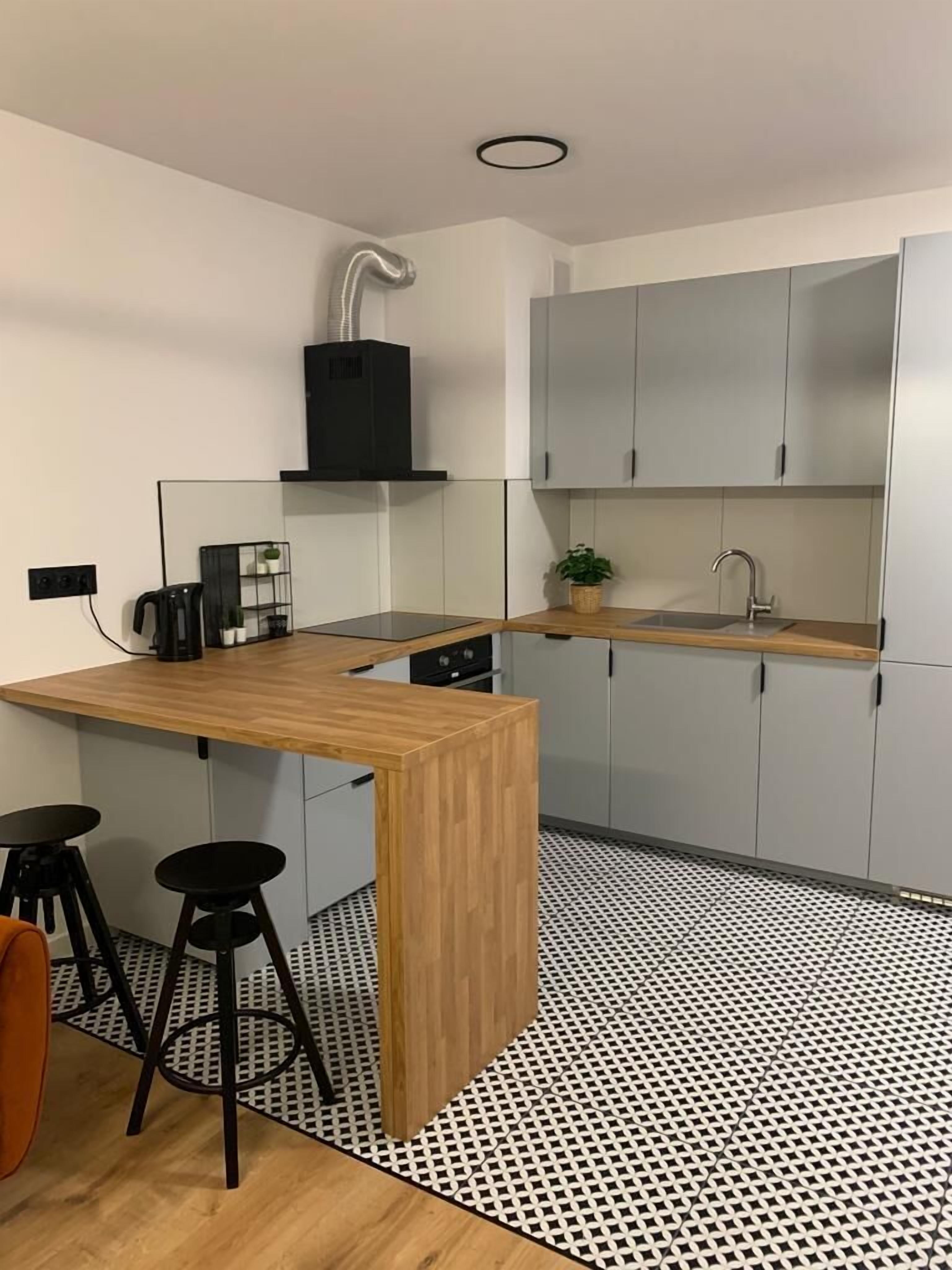 A modern kitchen with a wooden island, two black stools, a sink, and a black range hood.