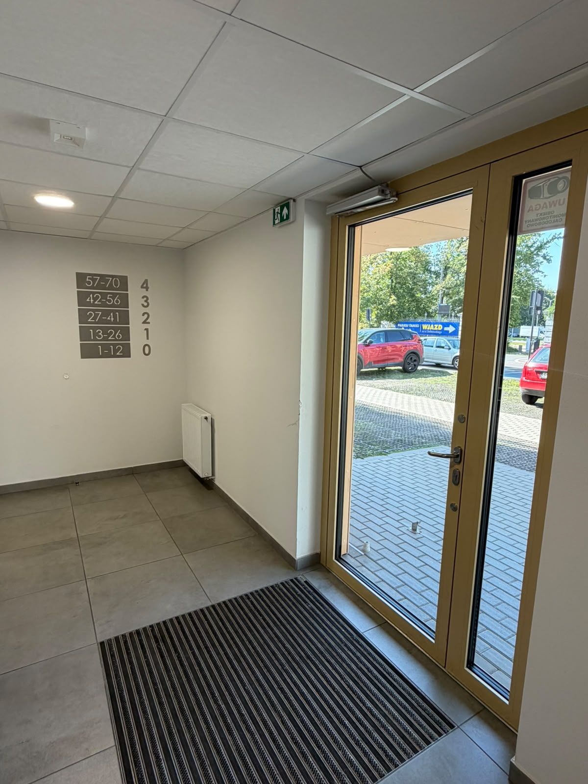 A hotel entrance with a glass door, a tiled floor, a vent, and a wall with room numbers.