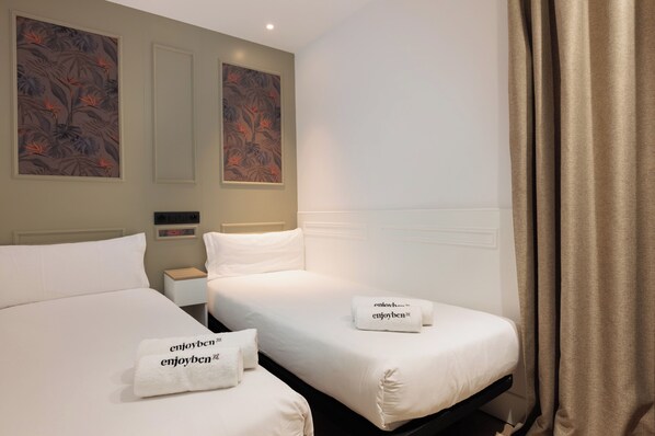 Habitación de hotel con dos camas, ropa de cama blanca y dos toallas con el texto "enjoyben".