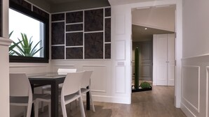 Un comedor con una mesa y sillas, una ventana con una planta y un pasillo que conduce a una habitación con un cactus.