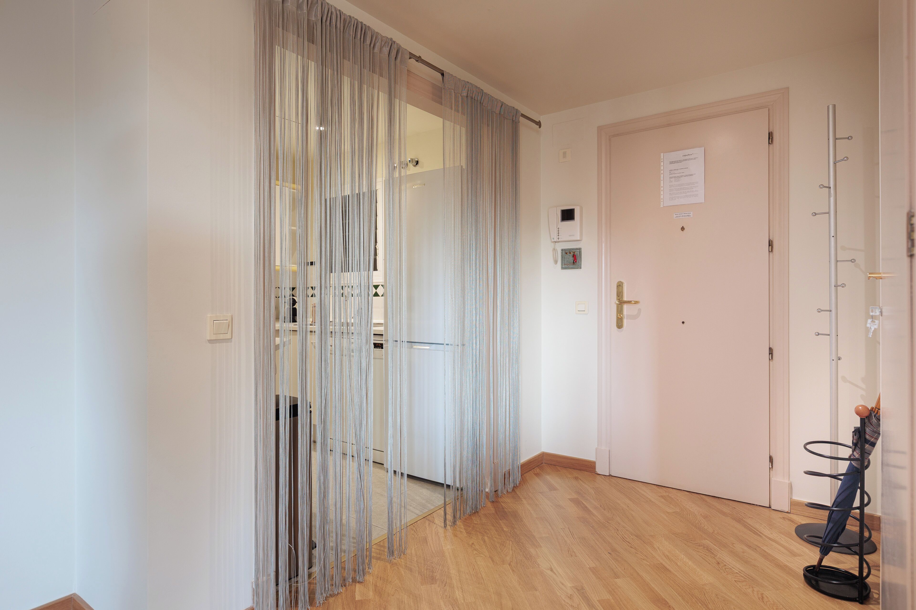 A hallway with a wooden floor, a door with a sign, and a coat rack with a bag.