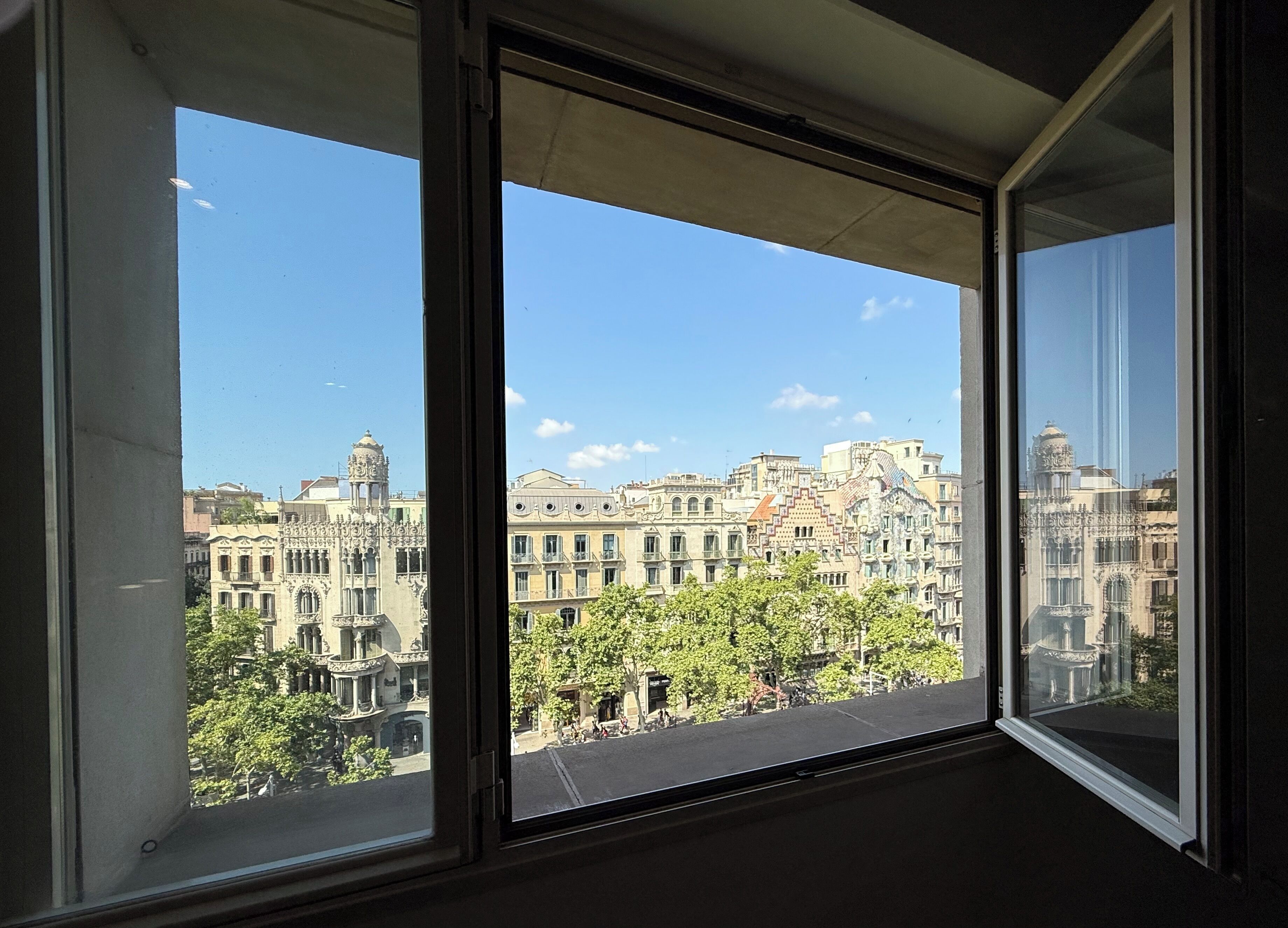 A view from a window with a clear sky, showcasing a cityscape with historic buildings and trees.