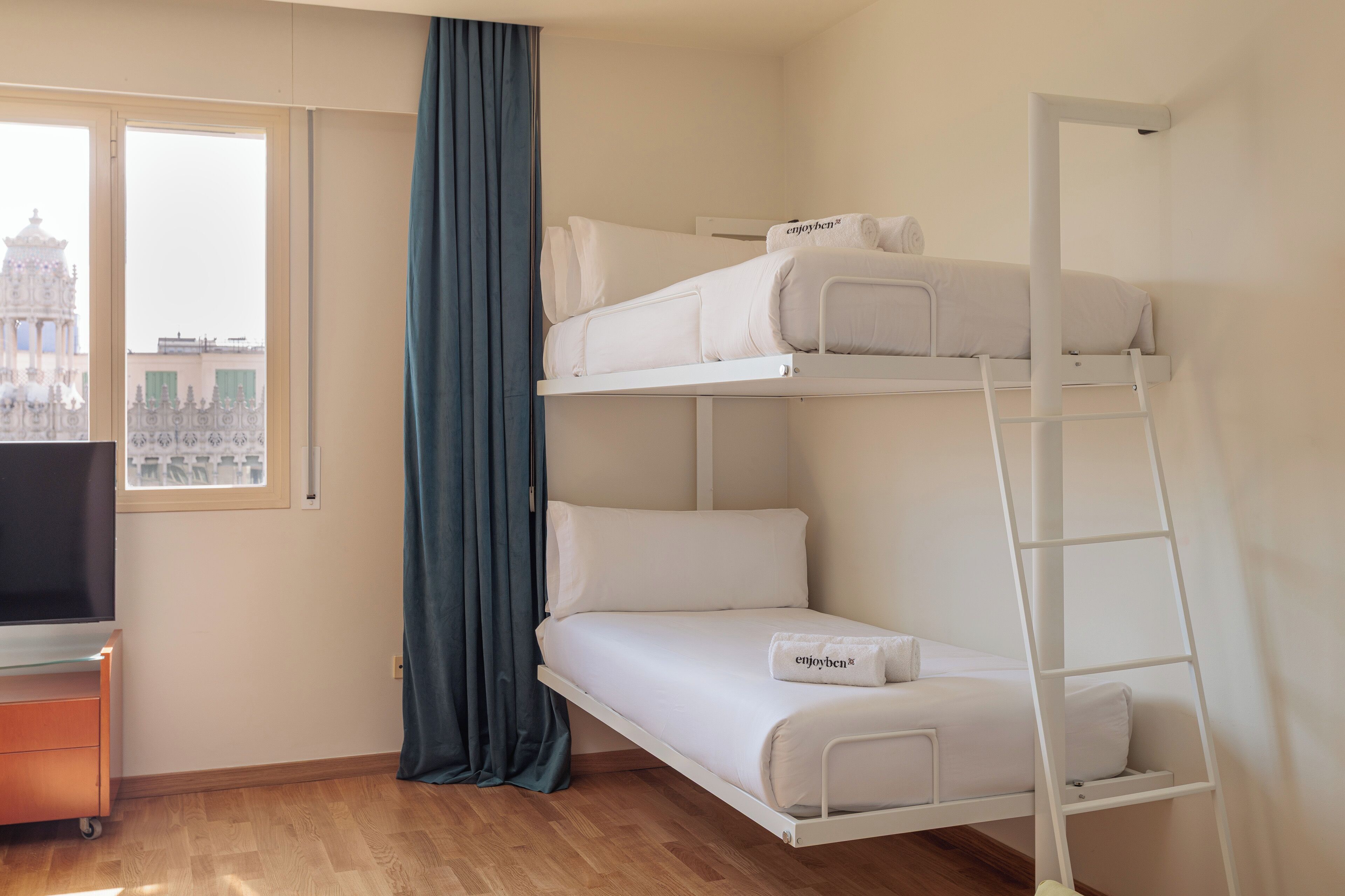 Una cama litera con un televisor y una ventana que ofrece vista a un edificio.