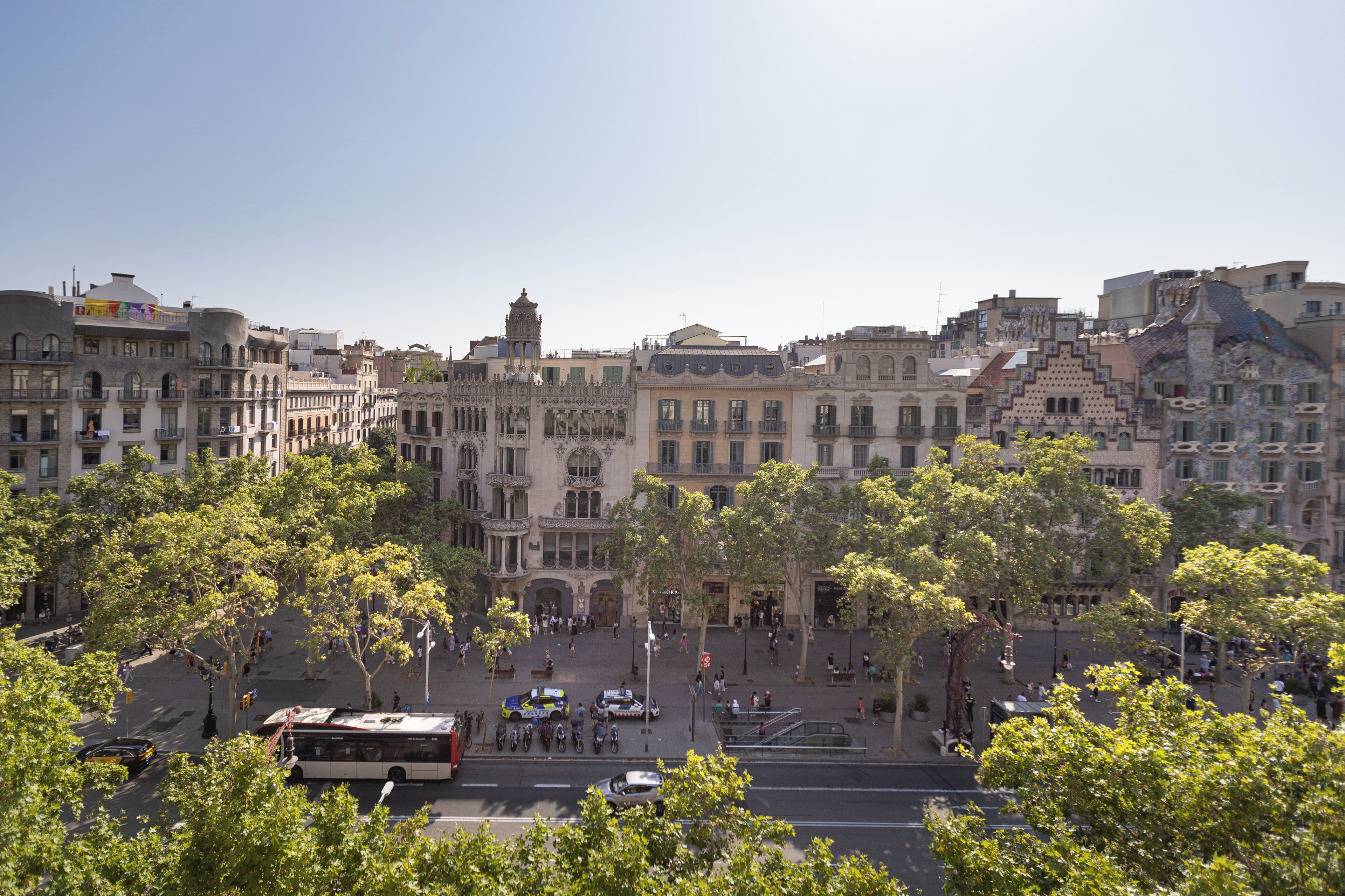 A historic city square with ornate buildings, a central fountain, and a bus in the foreground.