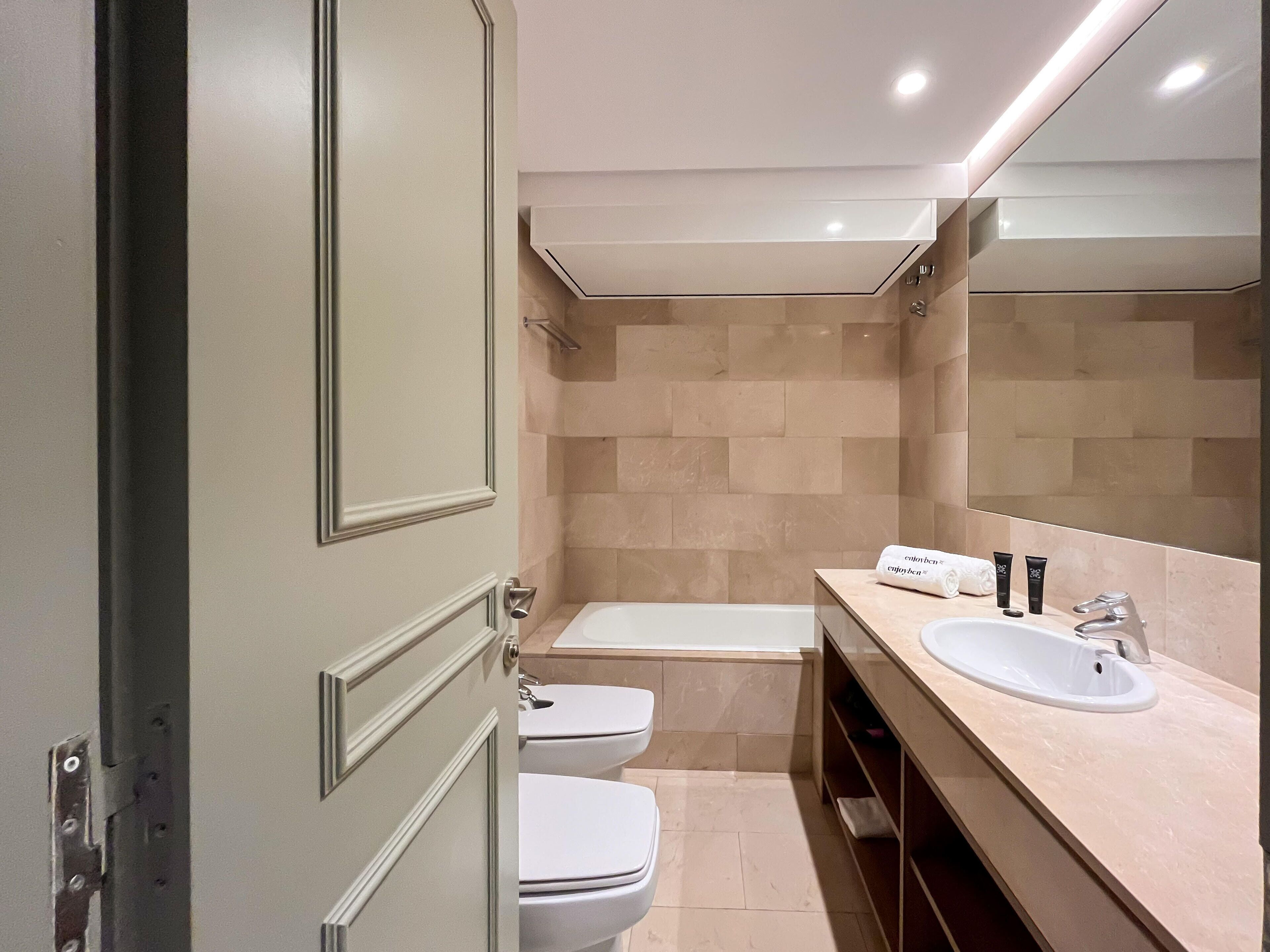 A modern bathroom with a double sink, a bathtub, and a toilet.