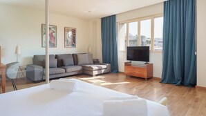Habitación de hotel con una cama grande, un sofá, un televisor y una ventana con cortinas.