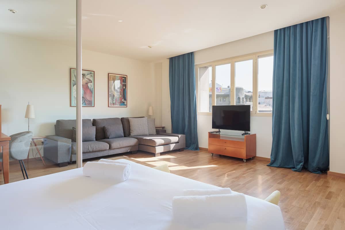 Habitación de hotel con una cama grande, un sofá, un televisor y una ventana con cortinas.