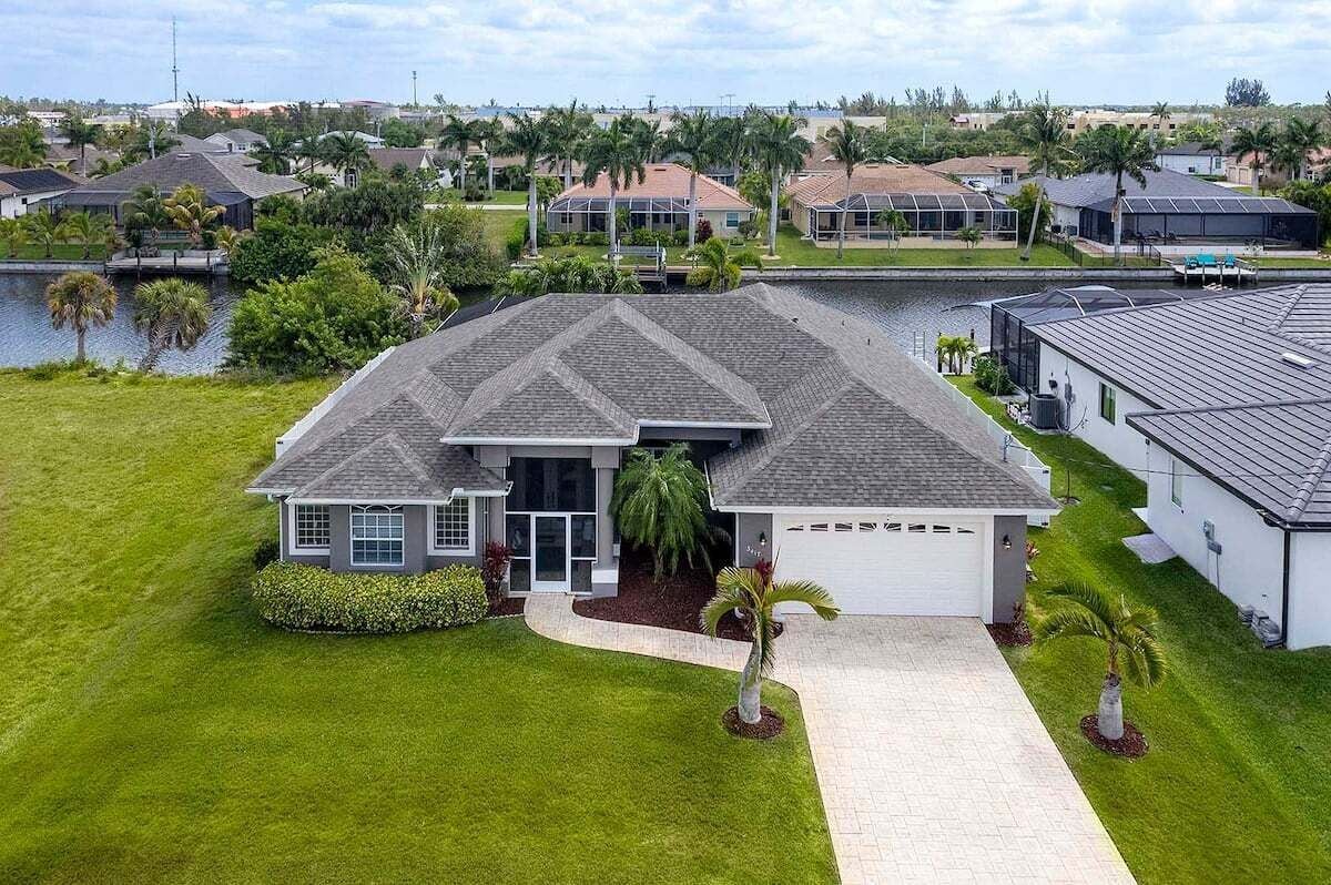 A modern house with a large driveway, a well-maintained lawn, and a body of water in the background.