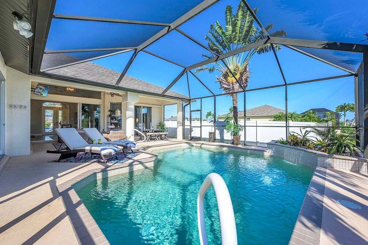 A pool area with clear blue water, a covered section with a glass ceiling, and a palm tree visible through the structure.