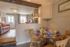 A dining area with a wooden table set for breakfast, a sofa in the background, and a view of the kitchen. - Burnham Cottage (2) , Well-next-the-Sea, Norfolk (Wells-next-the-Sea)