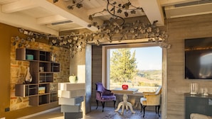 A modern living room with a stone wall, a large window, and a view of the outdoors. - Villa Etru (Peccioli)