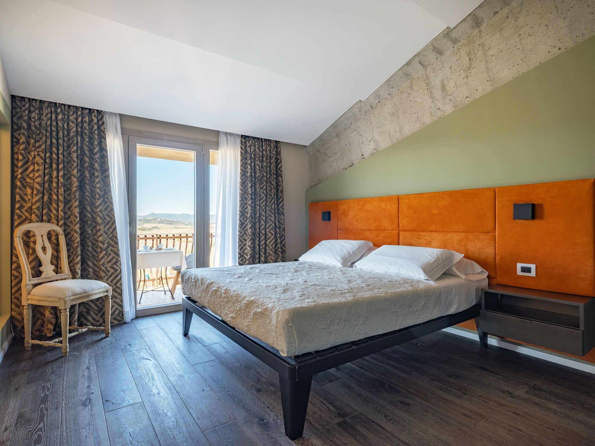 A bedroom with a bed, a chair, a nightstand, and a view of the outdoors.