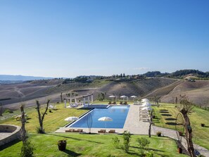 Zona de piscina con sillas de descanso y sombrillas, rodeada de un jardín ajardinado y vistas a colinas ondulantes.