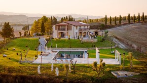 A large house with a swimming pool, surrounded by a well-maintained lawn and trees. - Villa Etru (Peccioli)