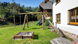 Un'altalena in legno, uno scivolo e una panca di legno in un giardino sul retro, con una casa sullo sfondo.