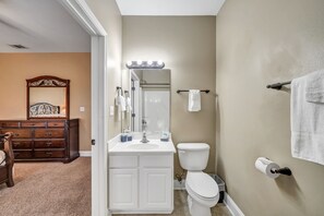 A bathroom with a white vanity, a toilet, and a mirror with lights. There is a wooden dresser in the adjacent room. - 30A Getaway Too! (Santa Rosa Beach)