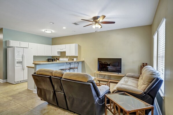 A living room with a reclining sofa, a flat-screen TV, and a ceiling fan. - 30A Getaway Too! (Santa Rosa Beach)