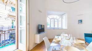 Un espace repas moderne avec une table en verre, des chaises blanches et un téléviseur posé sur un meuble blanc.