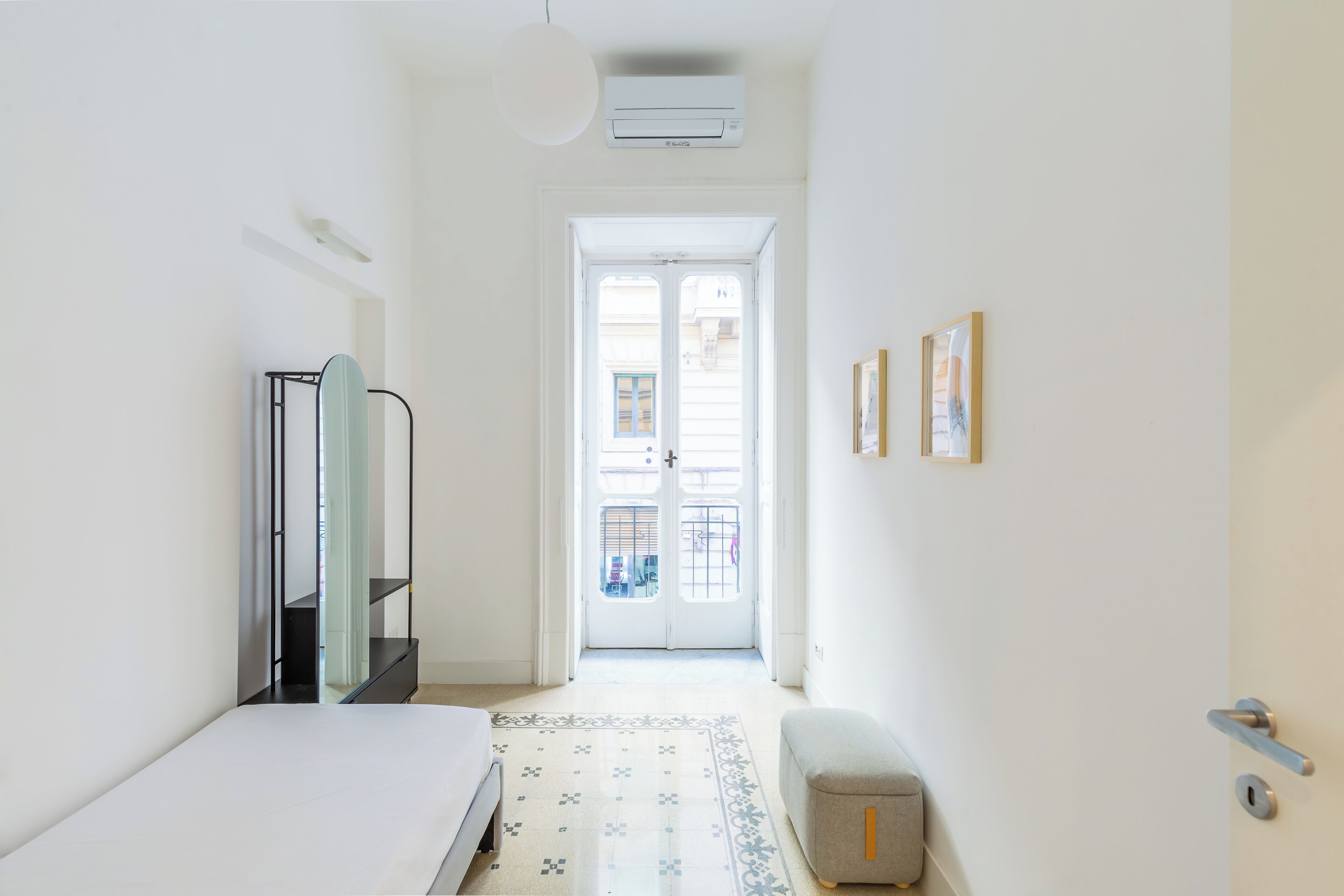 Una camera d'albergo con un letto, uno sgabello, un armadio, una porta che dà sull'esterno e un condizionatore d'aria a muro.