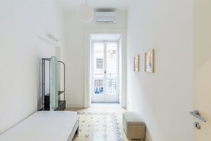 A hotel room with a bed, a small stool, a wardrobe, a door leading to the outside, and a wall-mounted air conditioning unit. - Amedeo Apartment by Wonderful Italy (Naples)