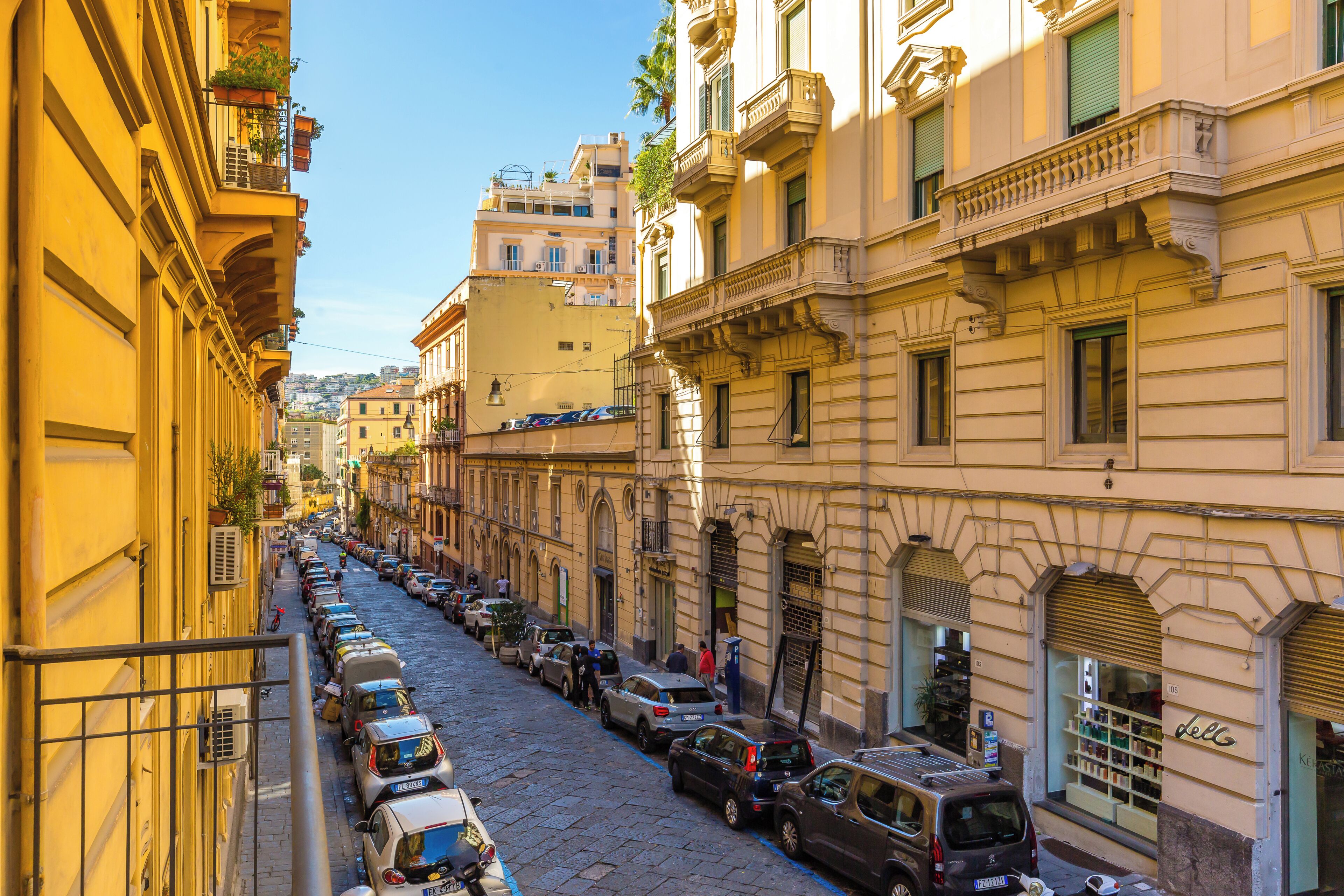Une rue étroite bordée de voitures garées et d’immeubles dotés de balcons.