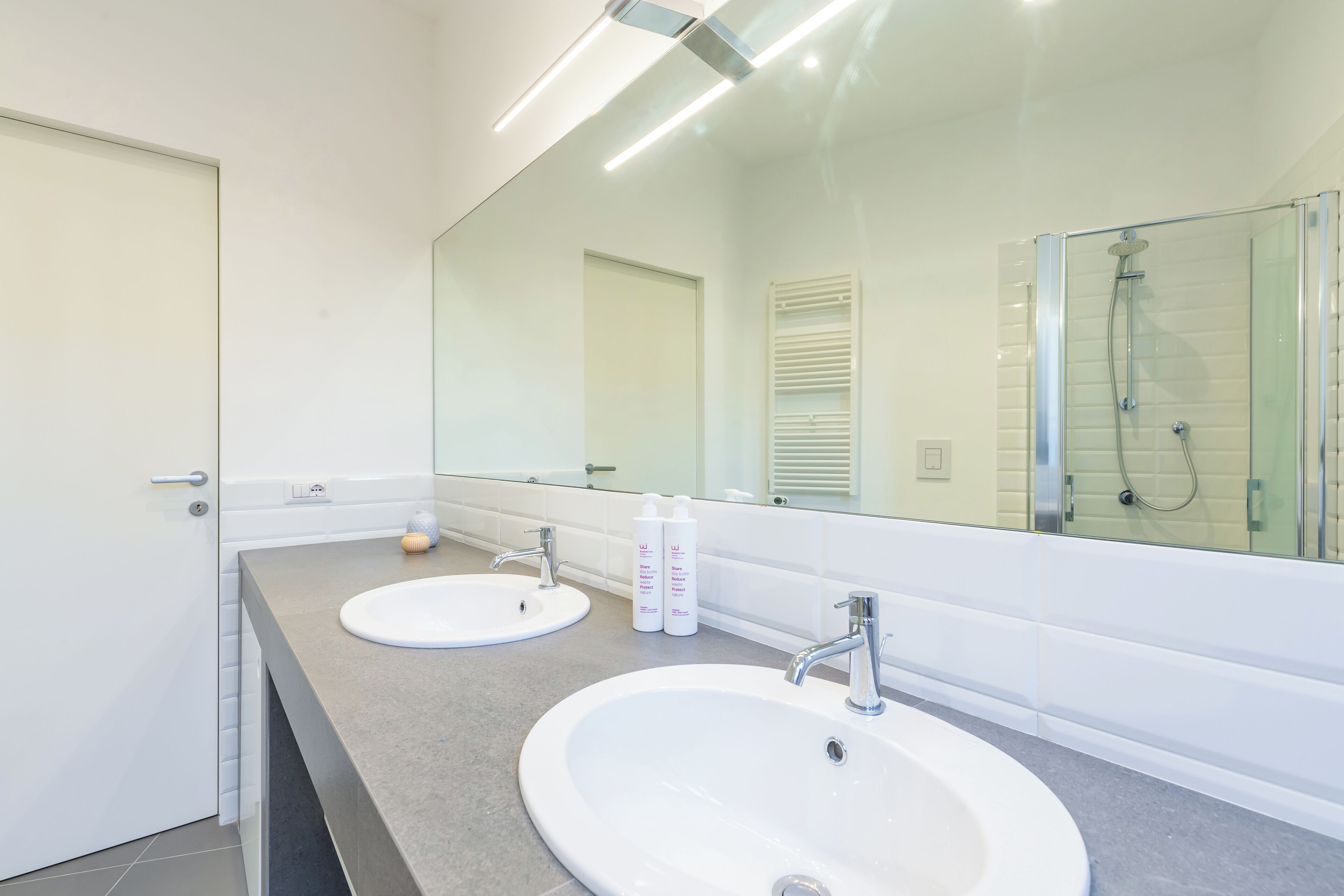 Une salle de bain moderne avec deux lavabos, un grand miroir et une douche à l’italienne.