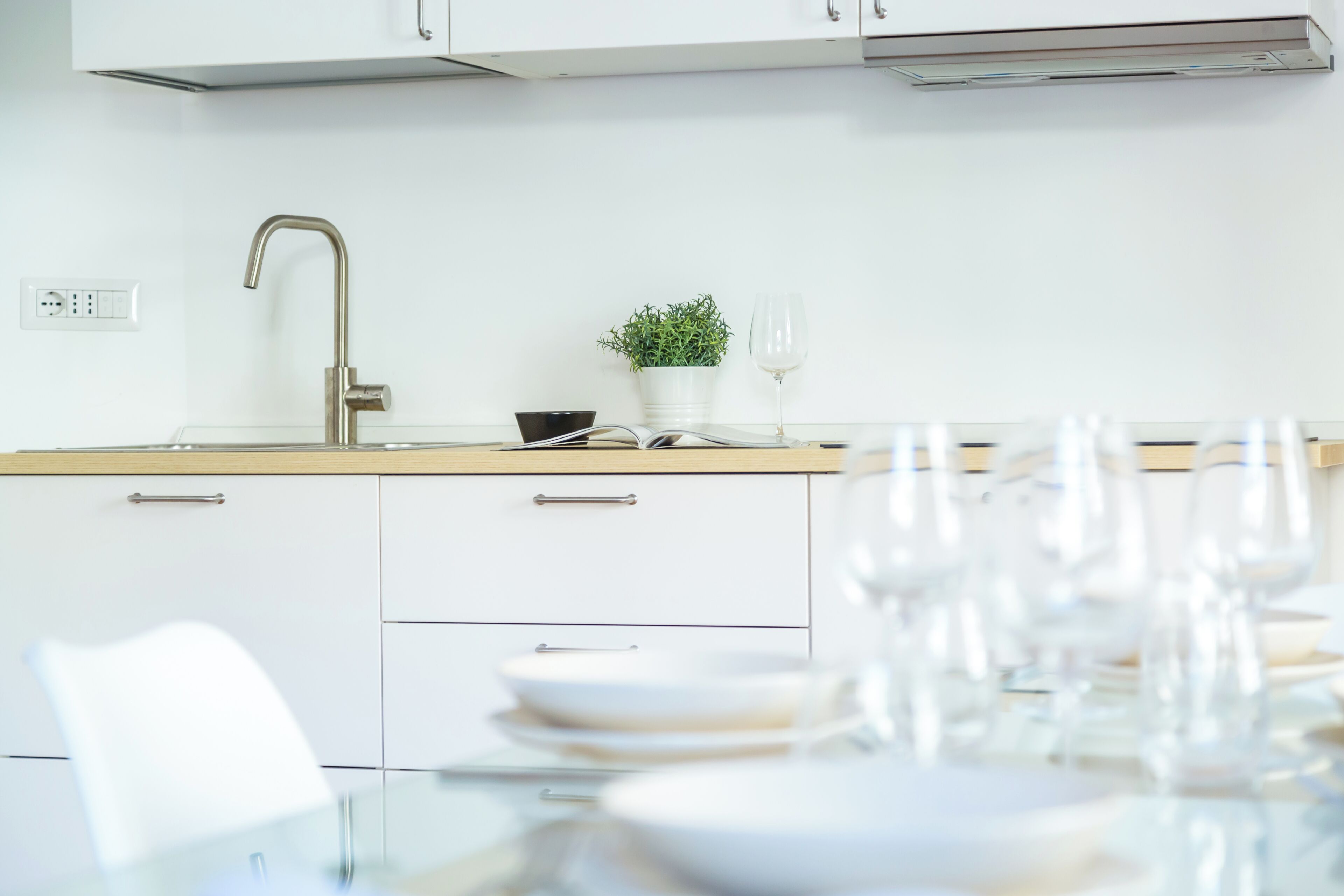 A modern kitchen with a stainless steel sink, white cabinets, and a dining area with a glass table set for a meal.