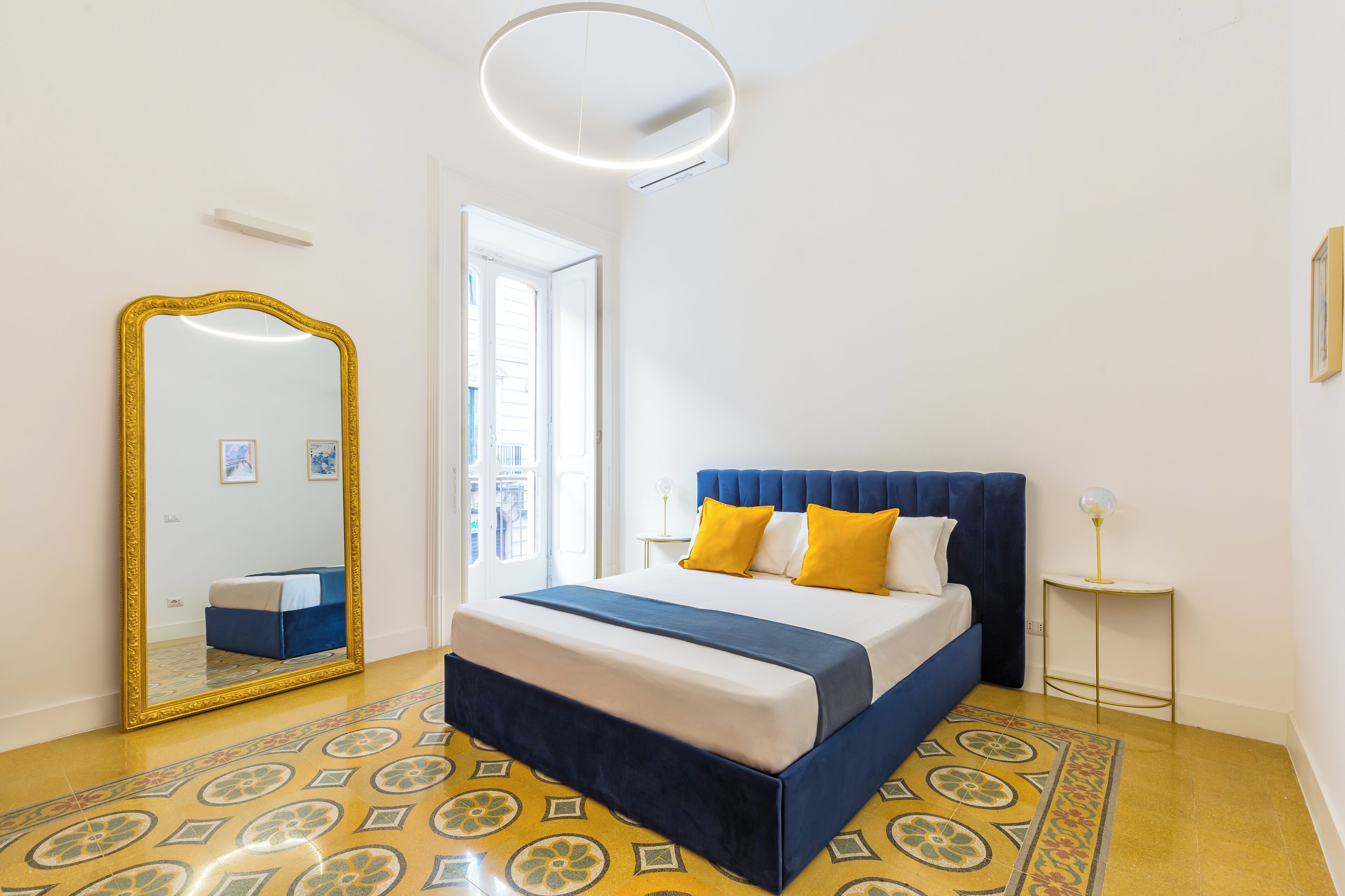 Un dormitorio con cama, un espejo grande, una mesita de noche y una lámpara de pie tipo globo.