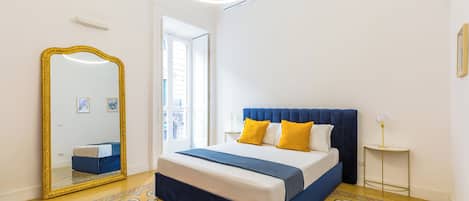 Un dormitorio con cama, un espejo grande, una mesita de noche y una lámpara de pie tipo globo.