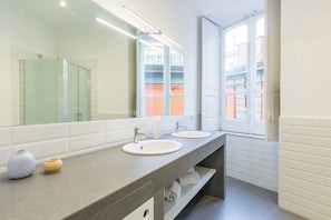 A modern bathroom with two sinks, a large mirror, and a window with a view of buildings.