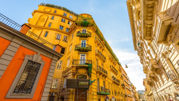Un immeuble jaune à plusieurs étages, doté de balcons et d’une entrée située à l’angle.