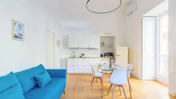 Um apartamento moderno com um sofá azul, sala de jantar com cadeiras e uma mesa posta para quatro pessoas, e cozinha com armários e eletrodomésticos brancos.