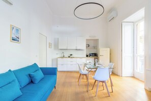 A modern living space with a blue sofa, a dining table with chairs, a kitchen area, and a large window. - Piazza Amedeo Flat by Wonderful Italy (Naples)