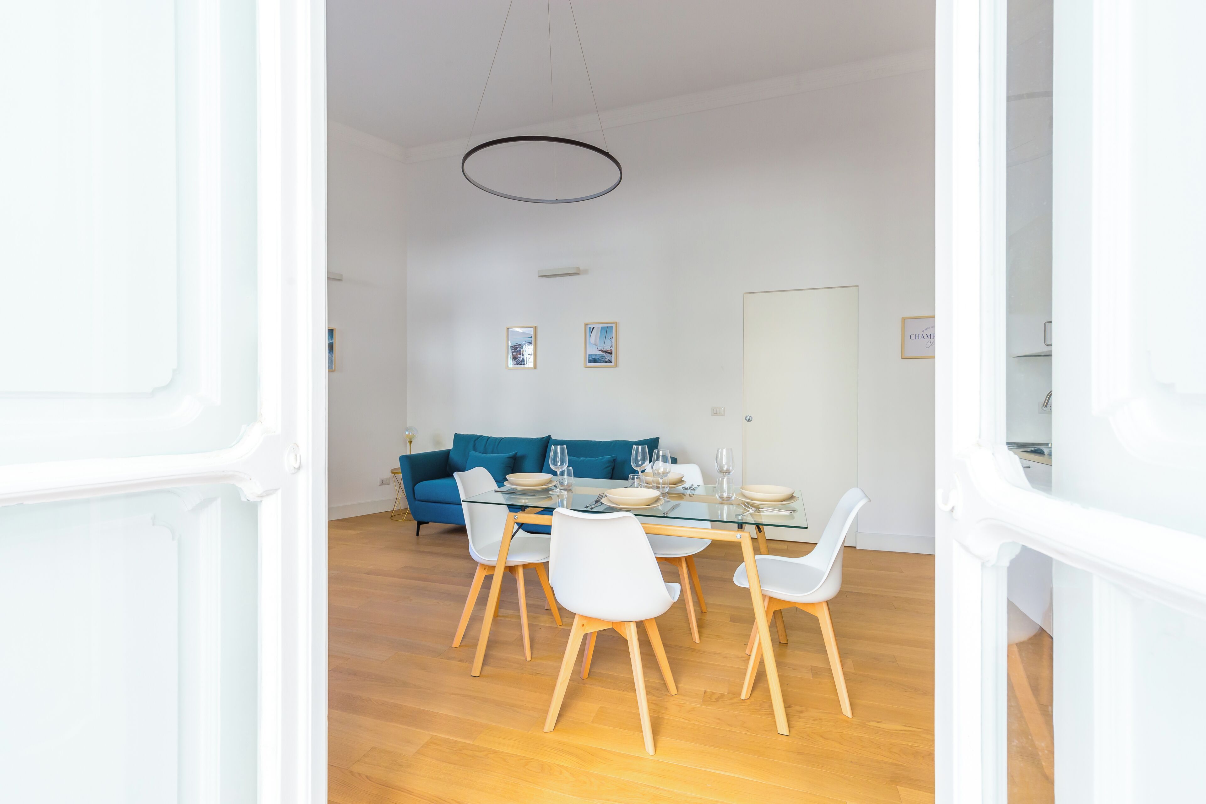 A modern dining area with a glass table, white chairs, and a blue sofa.