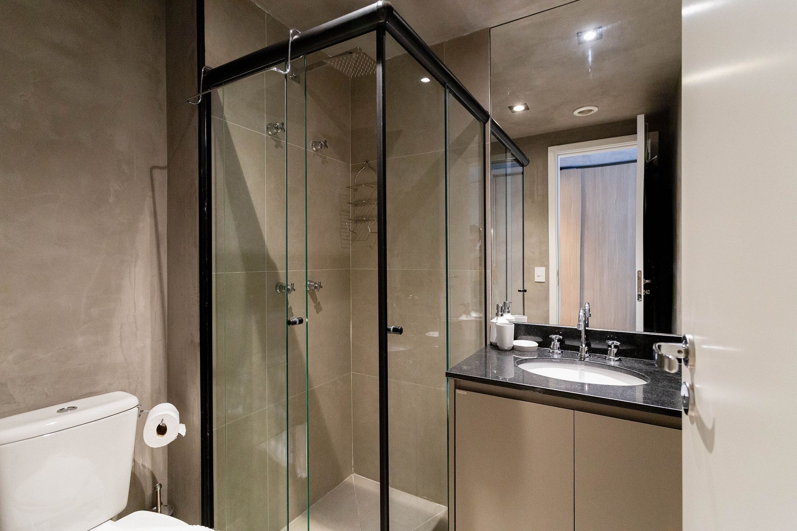 Un bany modern amb dutxa tancada amb vidre, un vàter blanc i un lavabo amb un mirall a sobre.