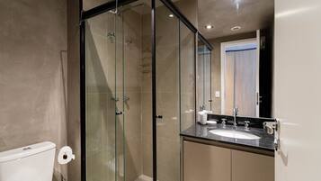 Un bany modern amb dutxa tancada amb vidre, un vàter blanc i un lavabo amb un mirall a sobre.