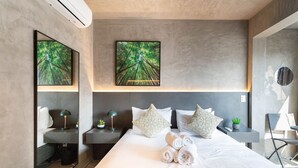 A modern hotel room with a large bed, two bedside tables, a mirror, and two framed artworks on the wall.