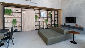 A modern living room with a sofa, a dining table with chairs, a coffee table, and a bookshelf with plants.