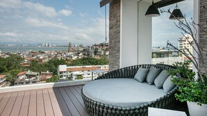 Ein Balkon mit einer runden Sitzecke, Blick auf eine Stadtlandschaft und ein Gewässer in der Ferne.