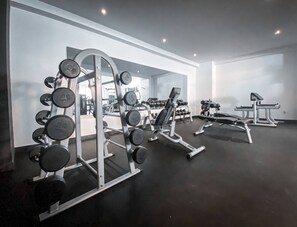 A gym with weightlifting equipment, including barbells and dumbbells, and a bench.