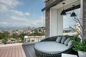 A balcony with a round seating area, a view of a cityscape, and a body of water in the distance. - Prime 2BR Condo, Rooftop Pool & Gym (Puerto Vallarta)