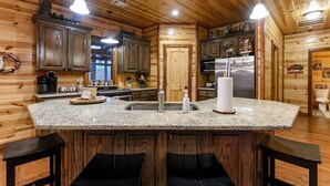 Cocina con paredes de madera, encimeras de granito, una isla central con taburetes de bar y electrodomésticos de acero inoxidable.
