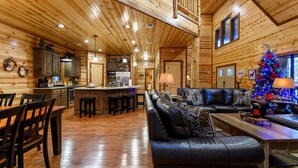 Interior de una cabaña de madera con comedor, cocina y un árbol de Navidad.